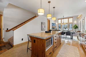 Kitchen featuring a kitchen bar, pendant lighting, light stone counters, brown cabinets, and a center island