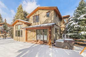 Snow covered property with a hot tub, stucco siding, and a metal roof