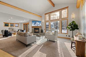 Living room featuring beamed ceiling, a fireplace, light carpet, and high vaulted ceiling