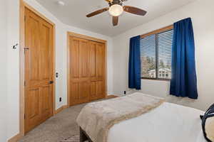 Carpeted bedroom with ceiling fan and a closet