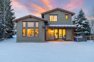 Snow covered back of property with stucco siding, a patio, and a metal roof