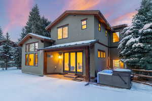 Snow covered back of property with a hot tub, a patio, french doors, stucco siding, and a metal roof
