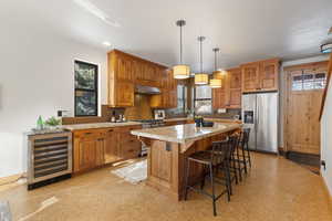 Kitchen with appliances with stainless steel finishes, brown cabinetry, a breakfast bar, beverage cooler, and recessed lighting
