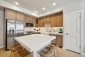 Kitchen featuring a kitchen bar, stainless steel appliances, brown cabinetry, light wood finished floors, and recessed lighting