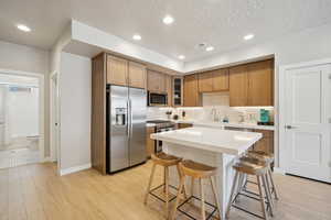 Kitchen featuring stainless steel appliances, a kitchen bar, brown cabinetry, a kitchen island, and glass insert cabinets
