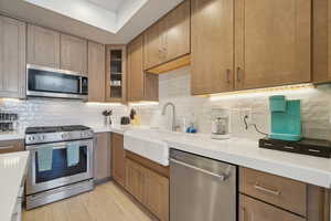 Kitchen featuring stainless steel appliances, glass insert cabinets, brown cabinetry, tasteful backsplash, and light wood-style floors