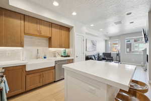Kitchen with brown cabinets, recessed lighting, decorative backsplash, a breakfast bar, and open floor plan