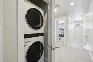 Laundry room featuring recessed lighting, estacked washer and dryer, and light carpet