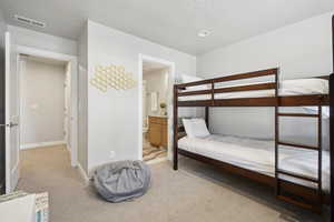 Bedroom with light carpet, connected bathroom, and a textured ceiling