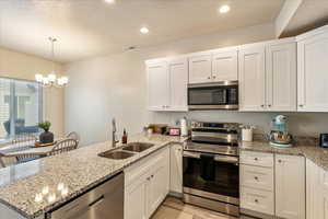 Kitchen featuring a peninsula, appliances with stainless steel finishes, white cabinets, light stone countertops, and a textured ceiling
