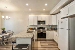 Kitchen featuring appliances with stainless steel finishes, a peninsula, white cabinetry, light stone counters, and recessed lighting