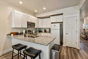 Kitchen with light stone countertops, white cabinets, stainless steel appliances, dark wood finished floors, and recessed lighting