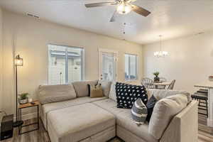 Living area with dark wood-style floors, a textured ceiling, healthy amount of natural light, a chandelier, and a ceiling fan