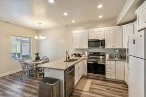 Kitchen featuring a peninsula, stainless steel appliances, a textured ceiling, white cabinets, and light stone countertops