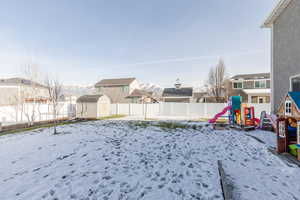 Yard covered in snow featuring a shed, a residential view, a fenced backyard, and a playground