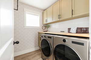 Laundry area featuring light wood finished floors, wallpapered walls, cabinet space, and washing machine and clothes dryer