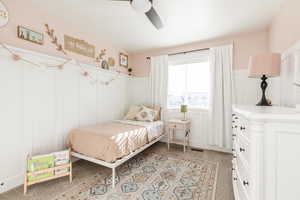 Bedroom featuring a decorative wall, wainscoting, a ceiling fan, and light carpet