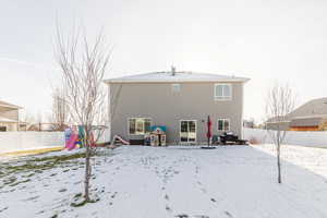 Snow covered back of property featuring a fenced backyard, a patio, and stucco siding