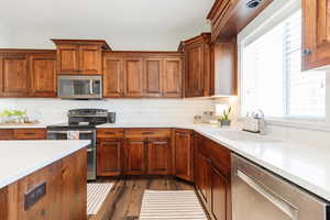 Kitchen featuring stainless steel appliances, light stone countertops, dark wood-type flooring, brown cabinets, and tasteful backsplash