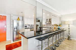 Kitchen with stainless steel fridge, a breakfast bar, a peninsula, ornamental molding, and white cabinets