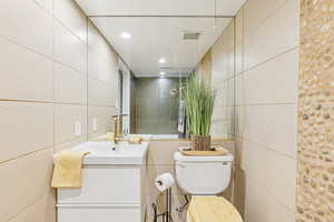 Full bath with tile walls, a tile shower, vanity, and recessed lighting