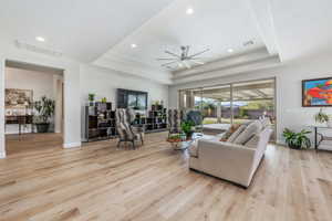 Living room with ceiling fan, light wood finished floors, a tray ceiling, and recessed lighting