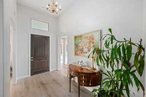 Entrance foyer with wood finished floors, a chandelier, and a towering ceiling