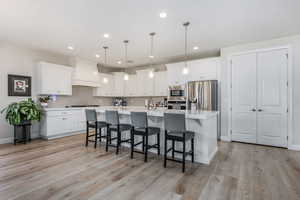Kitchen featuring a breakfast bar, a large island with sink, pendant lighting, stainless steel appliances, and white cabinets