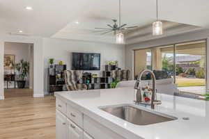 Kitchen with a raised ceiling, a ceiling fan, white cabinetry, light stone counters, and open floor plan