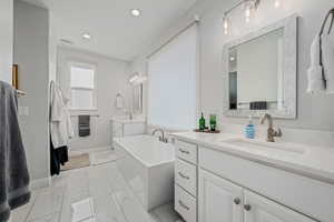 Bathroom with a freestanding tub, two vanities, light marble finish flooring, and recessed lighting