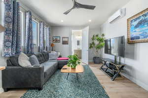 Living room featuring light wood-style floors, a wall mounted AC, a ceiling fan, and recessed lighting