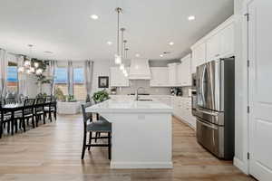 Kitchen with stainless steel appliances, recessed lighting, an island with sink, white cabinetry, and hanging light fixtures