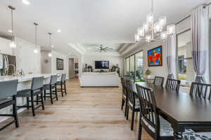 Dining space featuring a tray ceiling, light wood-style floors, ceiling fan, a chandelier, and recessed lighting