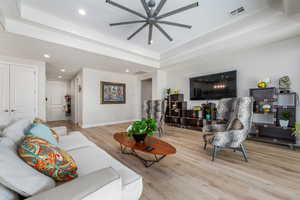 Living room with a raised ceiling, wood finished floors, ceiling fan, and recessed lighting