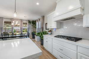 Kitchen featuring custom exhaust hood, hanging light fixtures, white cabinets, light stone counters, and light wood-type flooring
