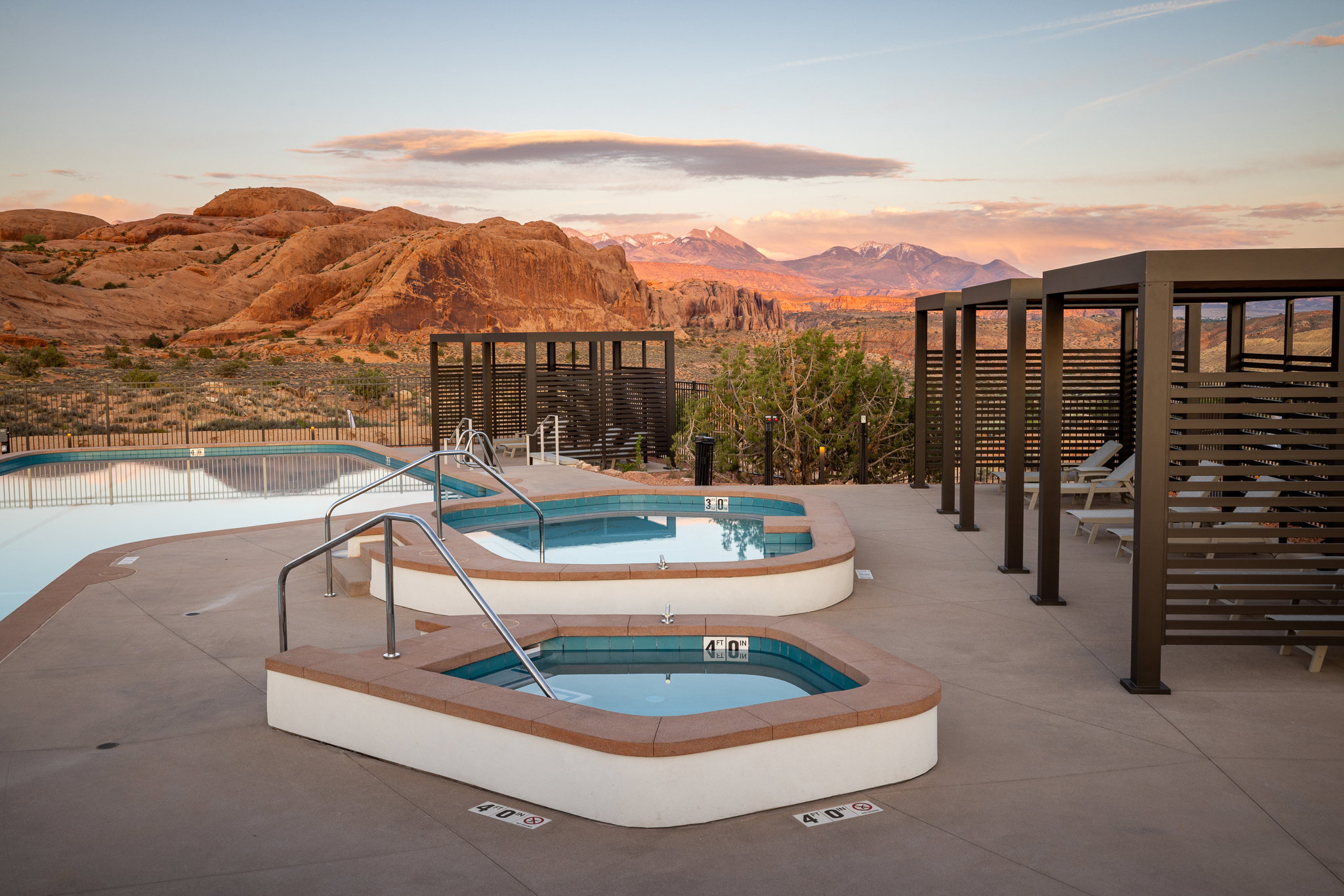 Outdoor amenity area featuring two spas, an adjacent swimming pool, multiple private cabanas, and desert landscaping