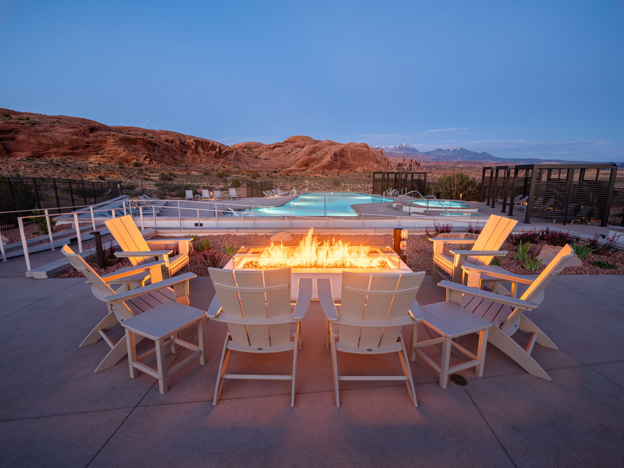 Outdoor fire pit area with Adirondack chairs, complemented by a swimming pool and hot tub, set against a desert landscape with distant mountains