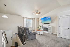 Living room with vaulted ceiling, carpet flooring, a glass covered fireplace, a textured ceiling, and ceiling fan