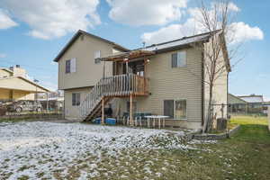 Snow covered house featuring a patio area, stairs, a wooden deck, and a gate