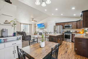 Kitchen featuring stainless steel appliances, dark brown cabinetry, a glass covered fireplace, lofted ceiling, and a center island