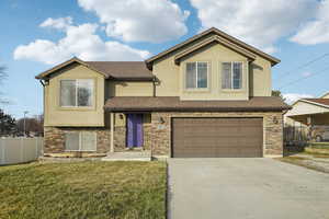 View of front of home with stucco siding, an attached garage, stone siding, and driveway