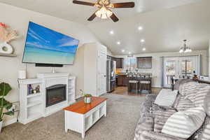 Living room with lofted ceiling, a glass covered fireplace, a chandelier, recessed lighting, and a ceiling fan
