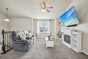Carpeted living room featuring a glass covered fireplace, a textured ceiling, and a ceiling fan