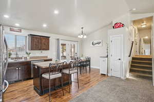 Kitchen featuring dark brown cabinetry, a center island, a breakfast bar, appliances with stainless steel finishes, and vaulted ceiling