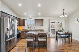 Kitchen featuring lofted ceiling, appliances with stainless steel finishes, dark brown cabinetry, light stone countertops, and recessed lighting