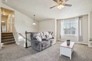 Living area featuring light carpet, a textured ceiling, stairway, ceiling fan, and lofted ceiling