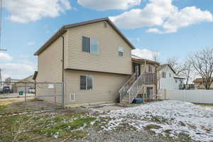 Snow covered back of property featuring a fenced backyard, stairs, a gate, and a patio