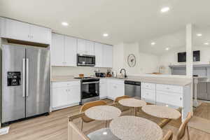Kitchen featuring stainless steel appliances, white cabinets, light wood-type flooring, recessed lighting, and vaulted ceiling