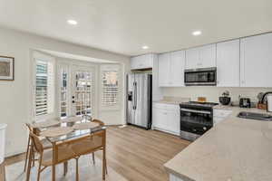 Kitchen with stainless steel appliances, light stone counters, white cabinetry, recessed lighting, and light wood-style floors