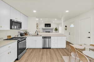 Kitchen featuring appliances with stainless steel finishes, vaulted ceiling, a peninsula, white cabinets, and light wood-type flooring